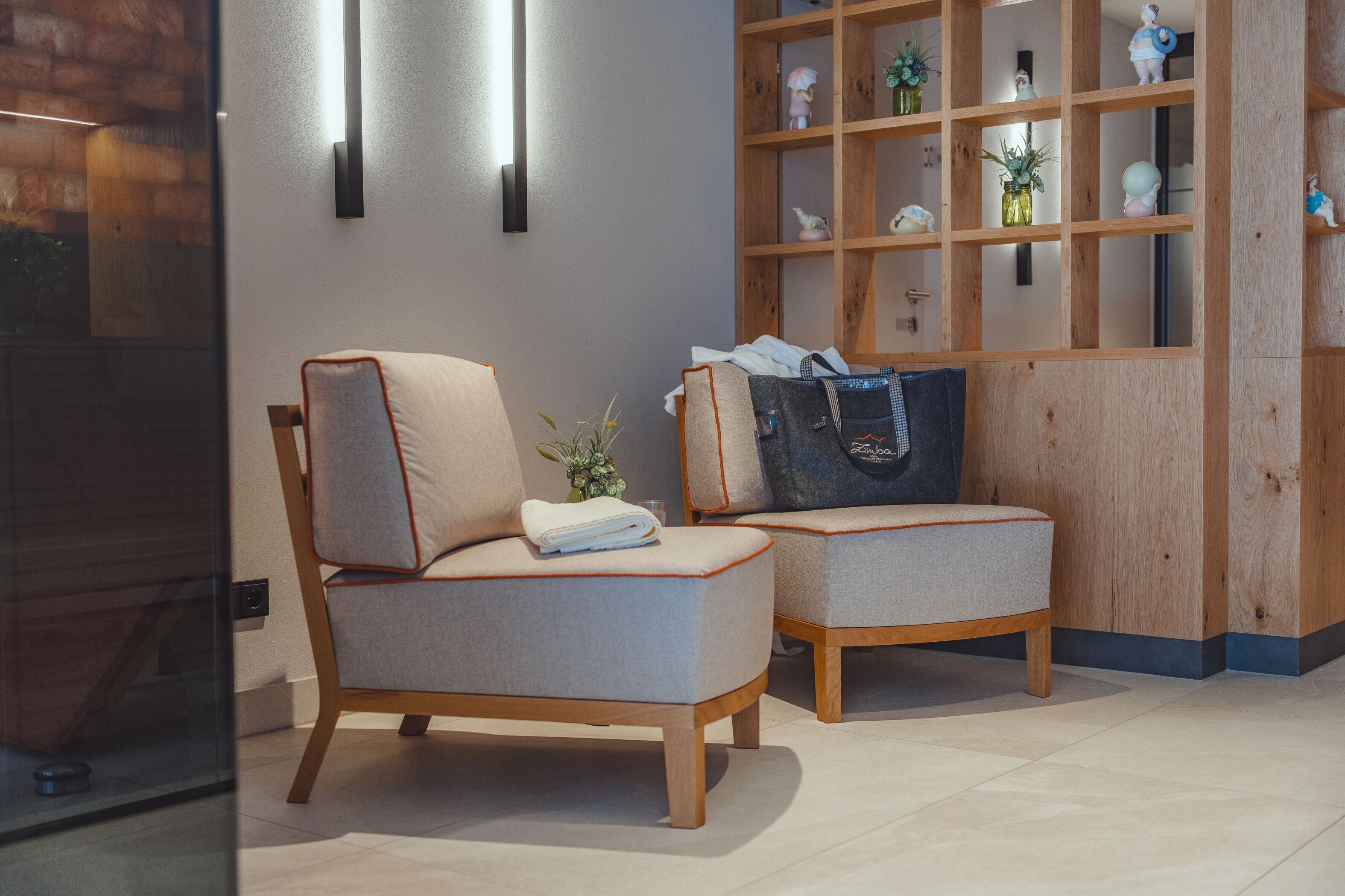 Een moderne kamer met twee fauteuils, een houten wandplank met decoratieve voorwerpen, en een glazen scheidingswand.