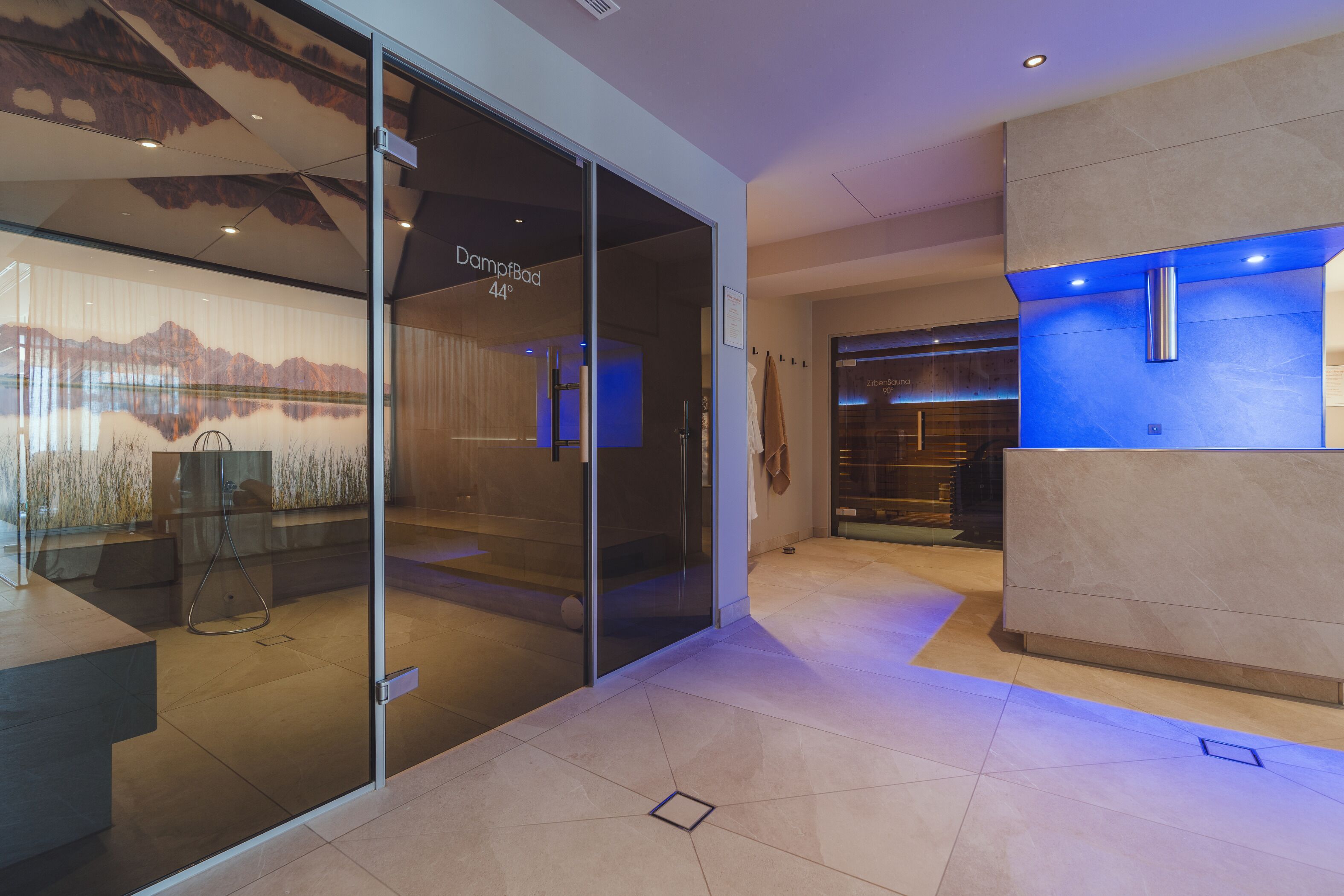 A modern hotel lobby with a glass wall displaying a mountain view, a reception desk, and a blue-lit wall.