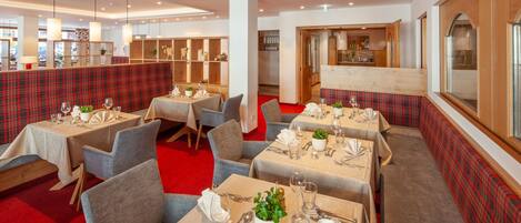 A restaurant with multiple tables set for dining, featuring red plaid booths and grey upholstered chairs.