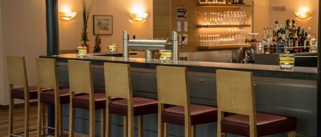 Un espace bar avec des tabourets de bar en bois, un comptoir et des étagères remplies de bouteilles et de verres.