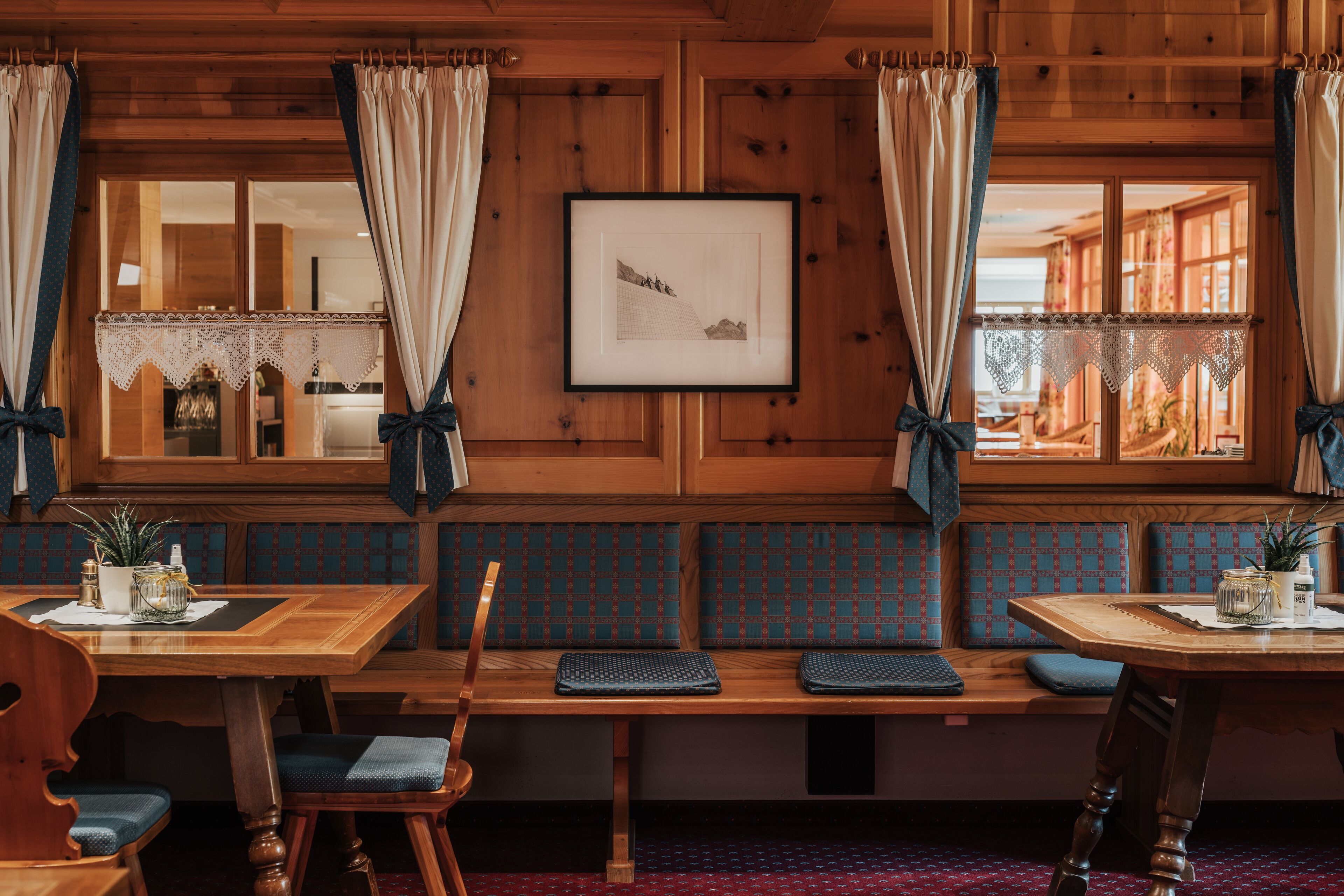 A wooden interior with a bench seating area, a framed picture on the wall, and a window with curtains.