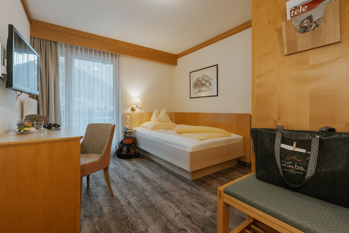 A hotel room with a bed, a desk, a chair, a TV, a lamp, and a wall-mounted bag.
