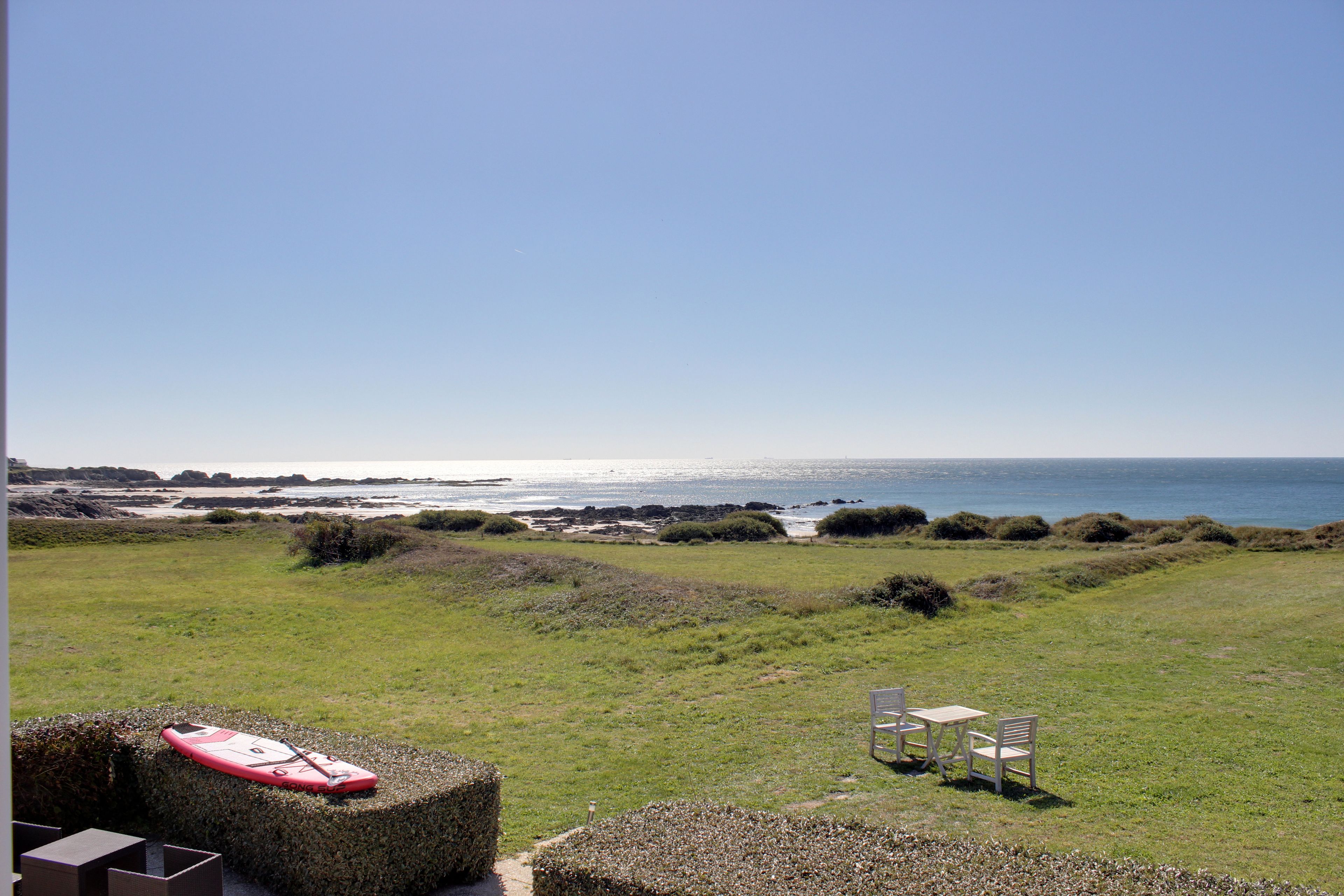 Un área con césped, una mesa, sillas, una tabla de remo roja y vistas al mar.