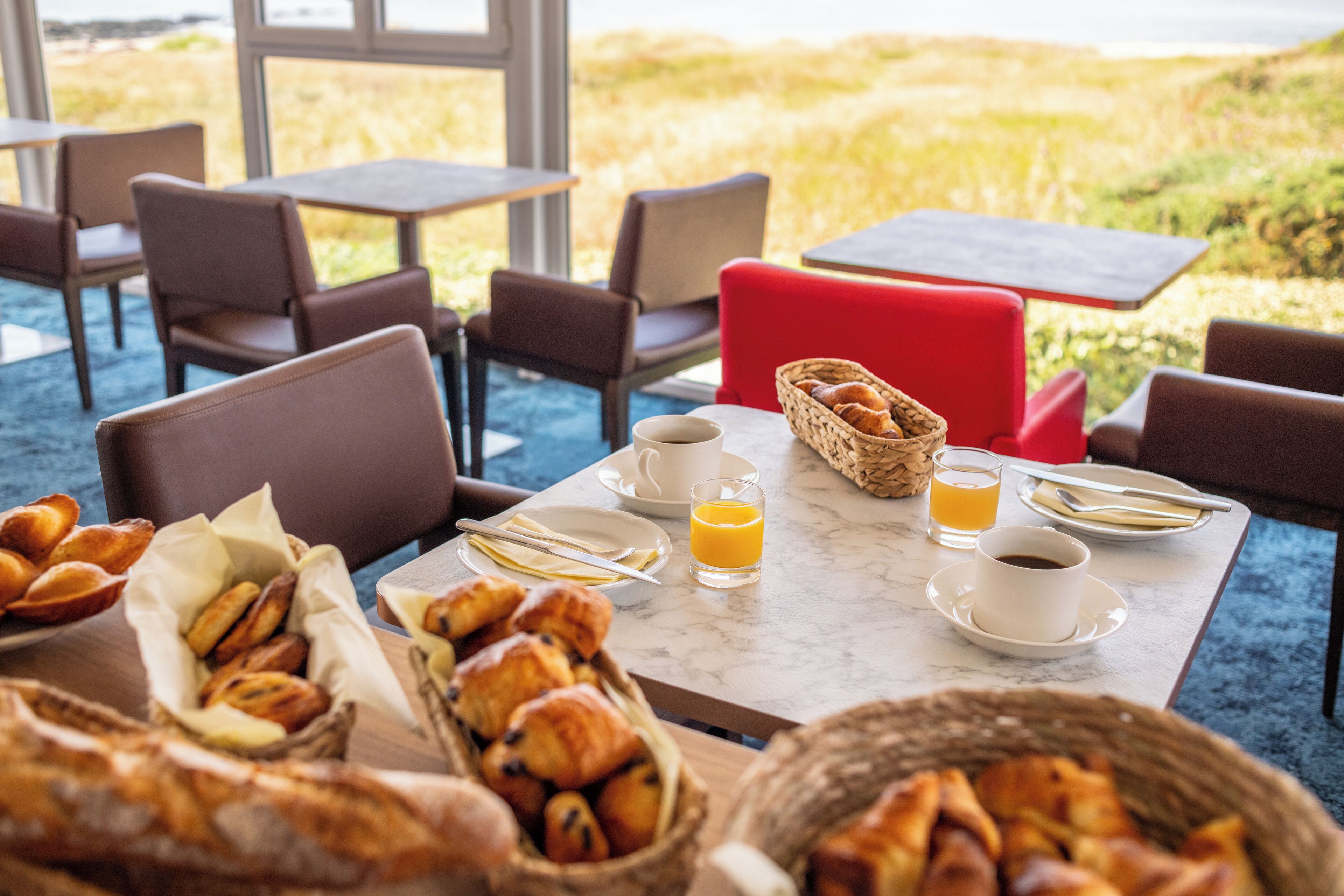 A breakfast setting with croissants, orange juice, and coffee on a table with a view of the beach.