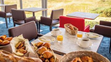 A breakfast setting with croissants, orange juice, and coffee on a table with a view of the beach.