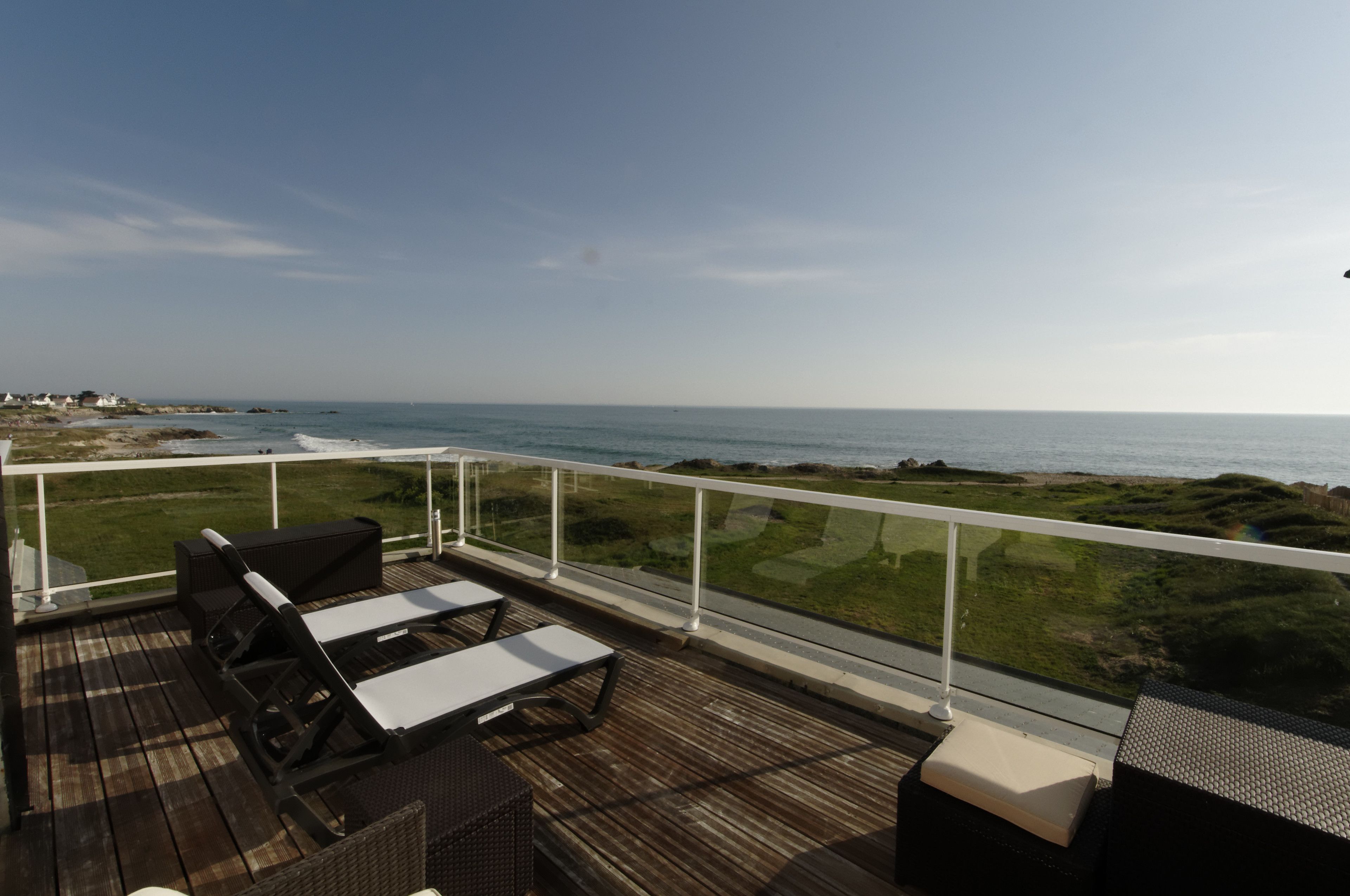 Una terraza de madera con mobiliario exterior y vistas al océano.
