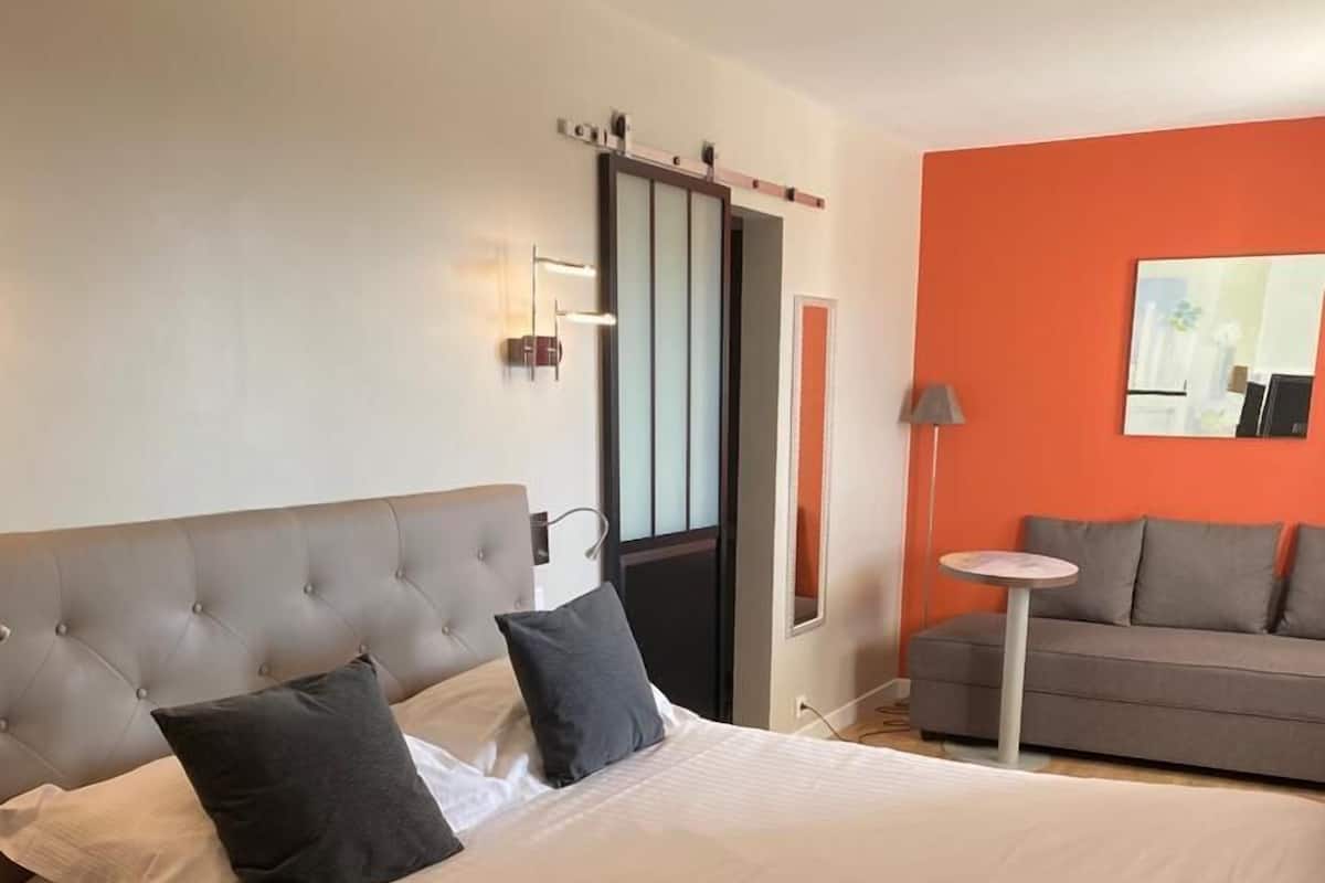 A modern hotel room with a large bed, a grey sofa, and a small round table.