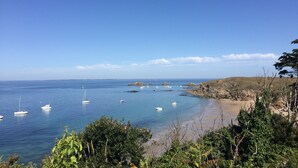 A coastal landscape with clear blue waters, boats, rocky shores, and greenery. - Hotel Le Lichen (Batz-sur-Mer)