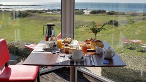A breakfast table with a view of the ocean, a coffee pot, a teapot, and a croissant. - Hotel Le Lichen (Batz-sur-Mer)