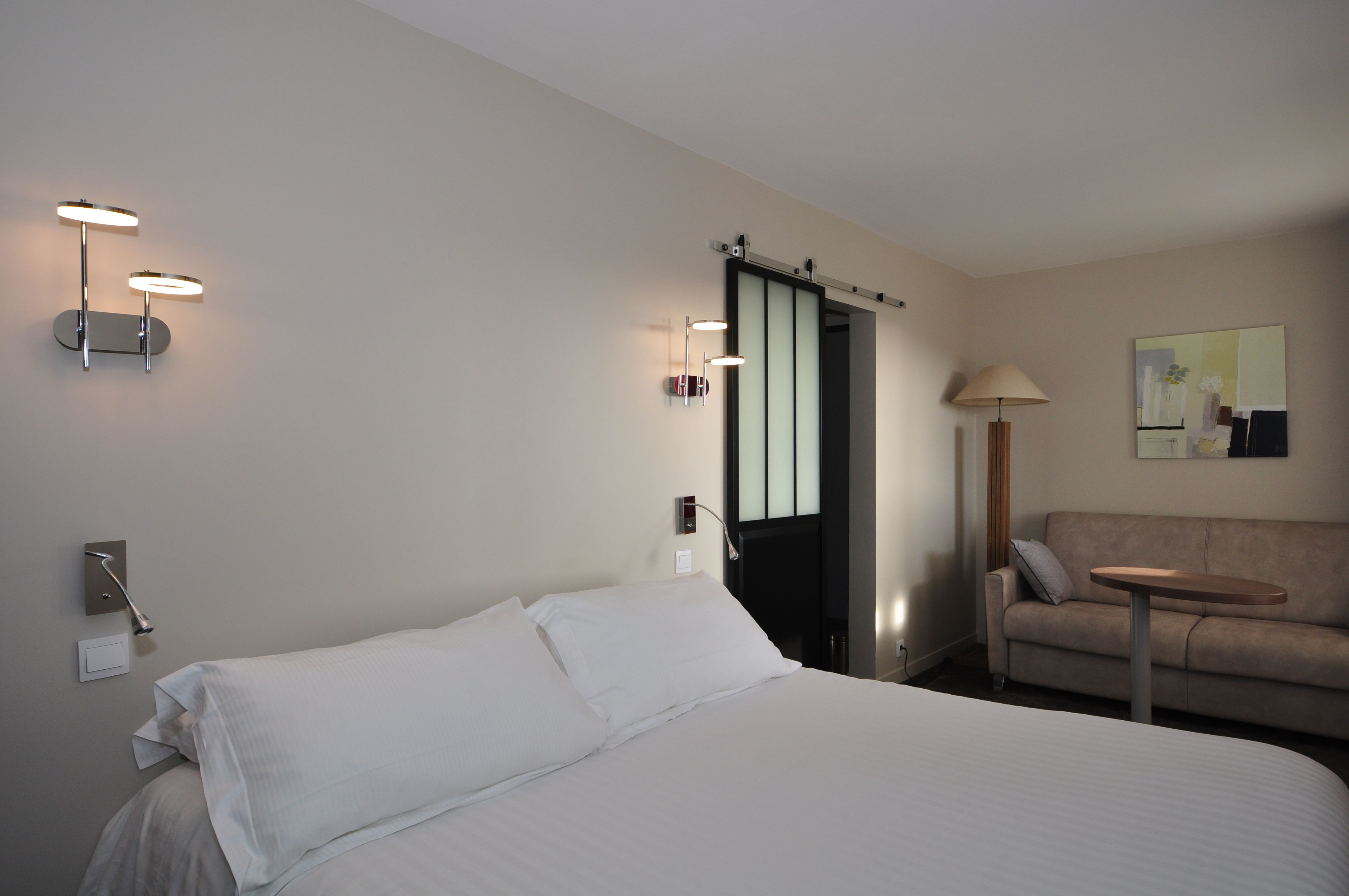 A hotel room with a bed, a sofa, a small table, and a door leading to a bathroom.