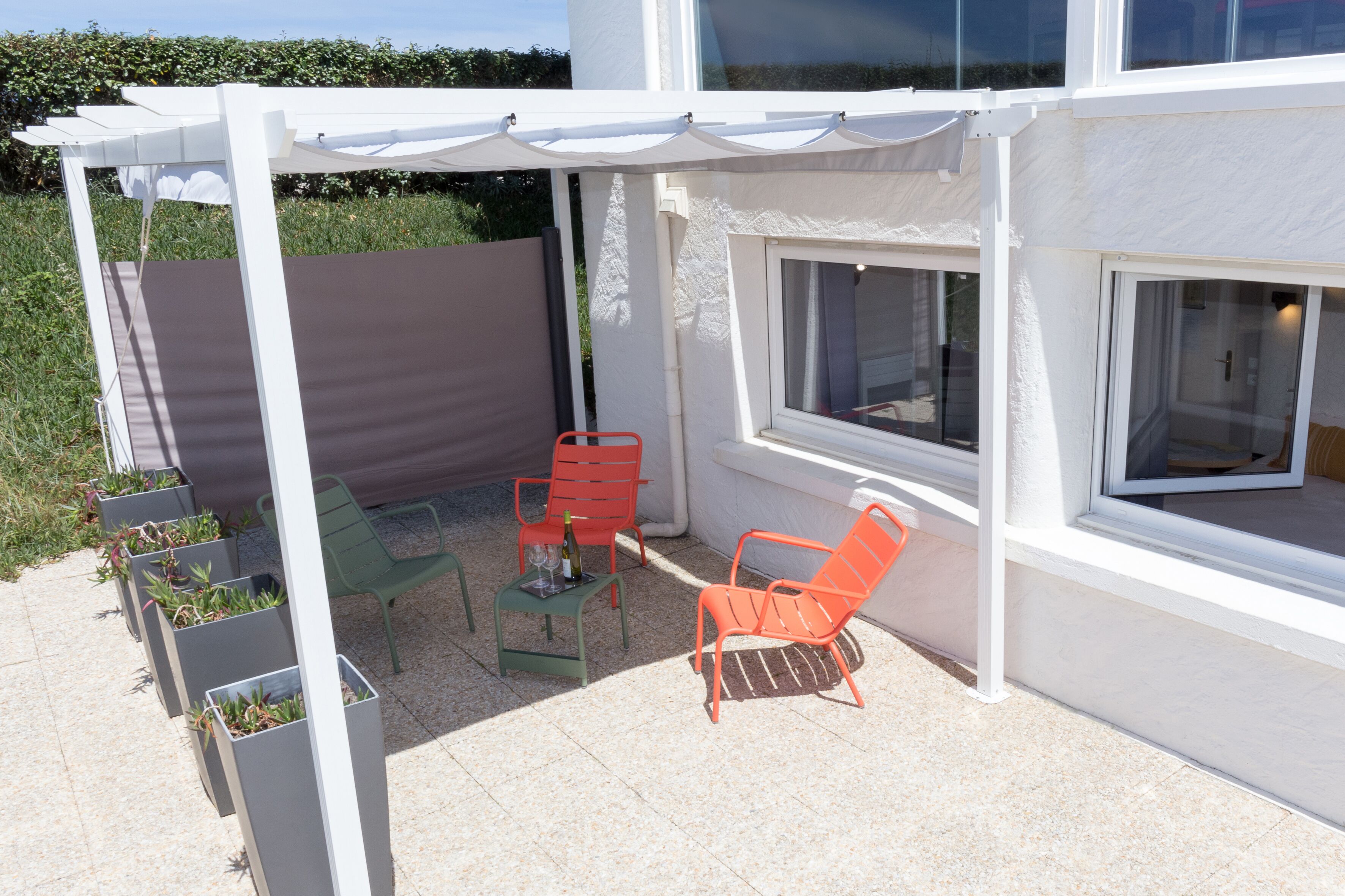 A covered patio area with two chairs and a table, surrounded by planters with plants.