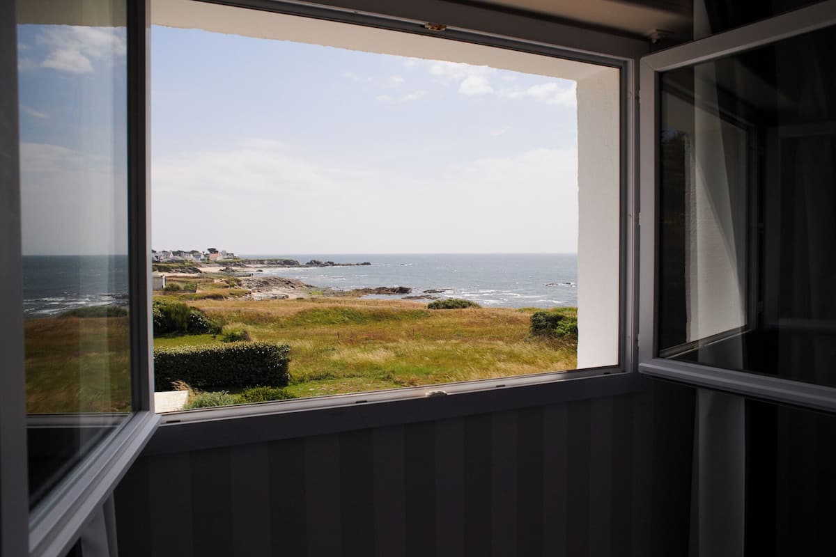 A coastal view through a window with a view of the sea, rocky shoreline, and grassy areas.