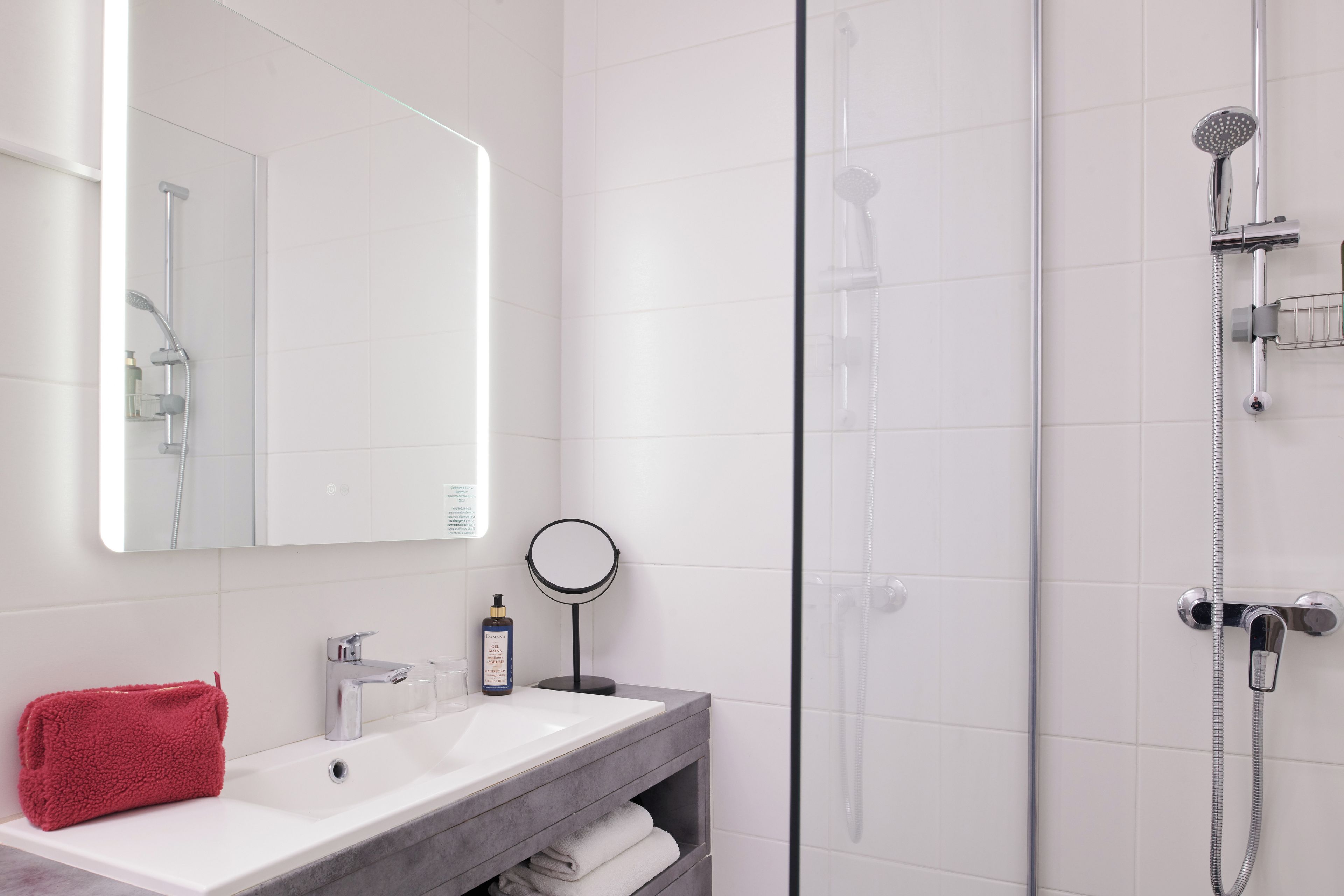 A modern bathroom with a white sink, a red towel, a mirror, and a glass-enclosed shower area.