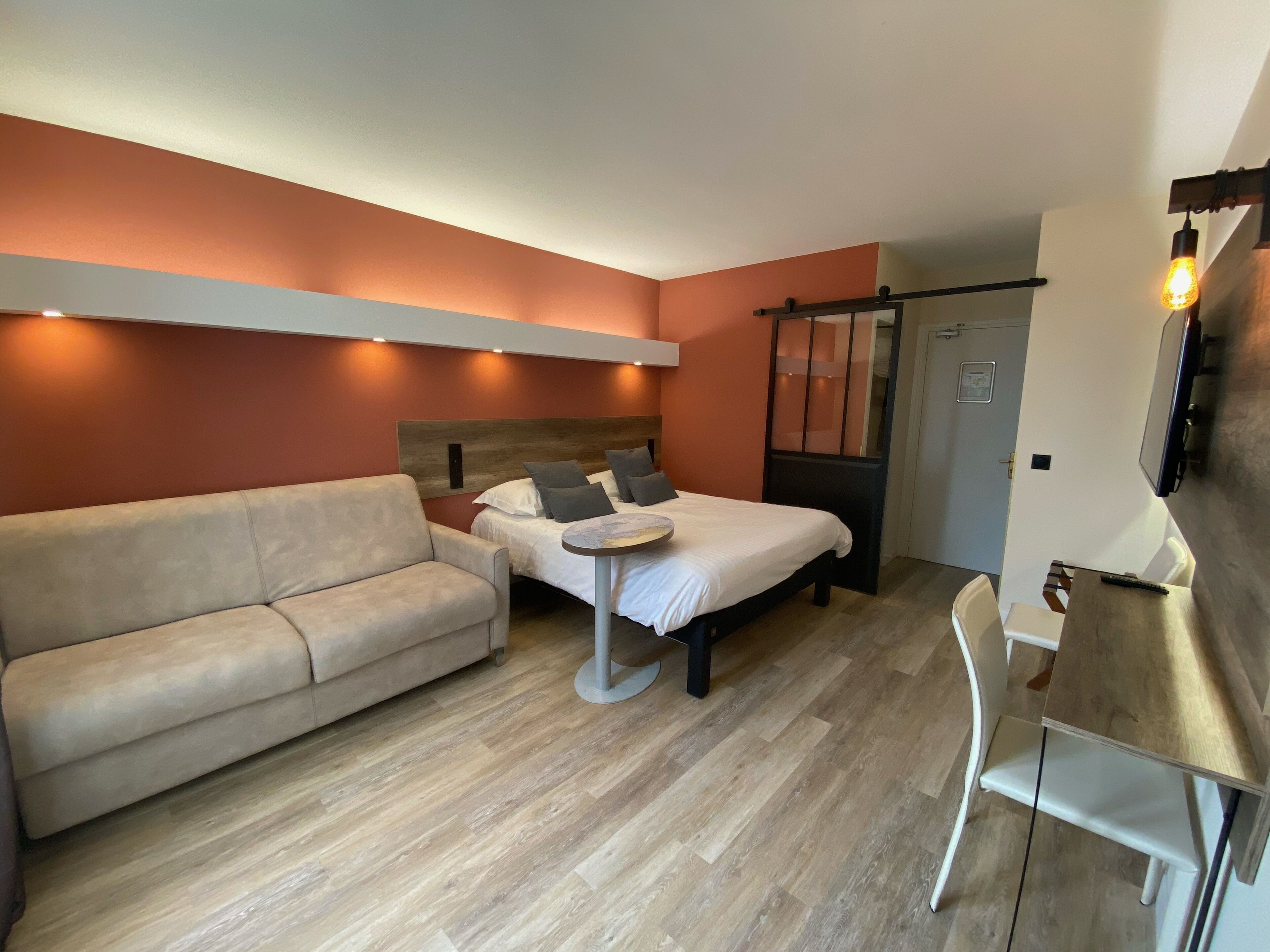 Un dormitorio moderno con cama, sofá, una mesita y televisor.