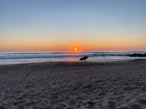 A beach at sunset with a surfer walking towards the water. - Hotel Le Lichen (Batz-sur-Mer)