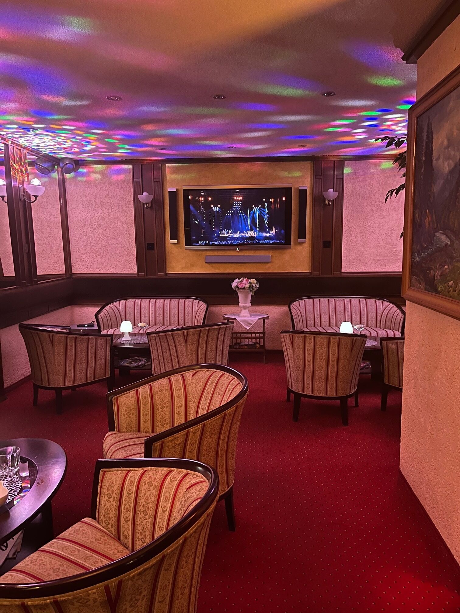 A room with a television, patterned chairs, a small table, and a red carpet.