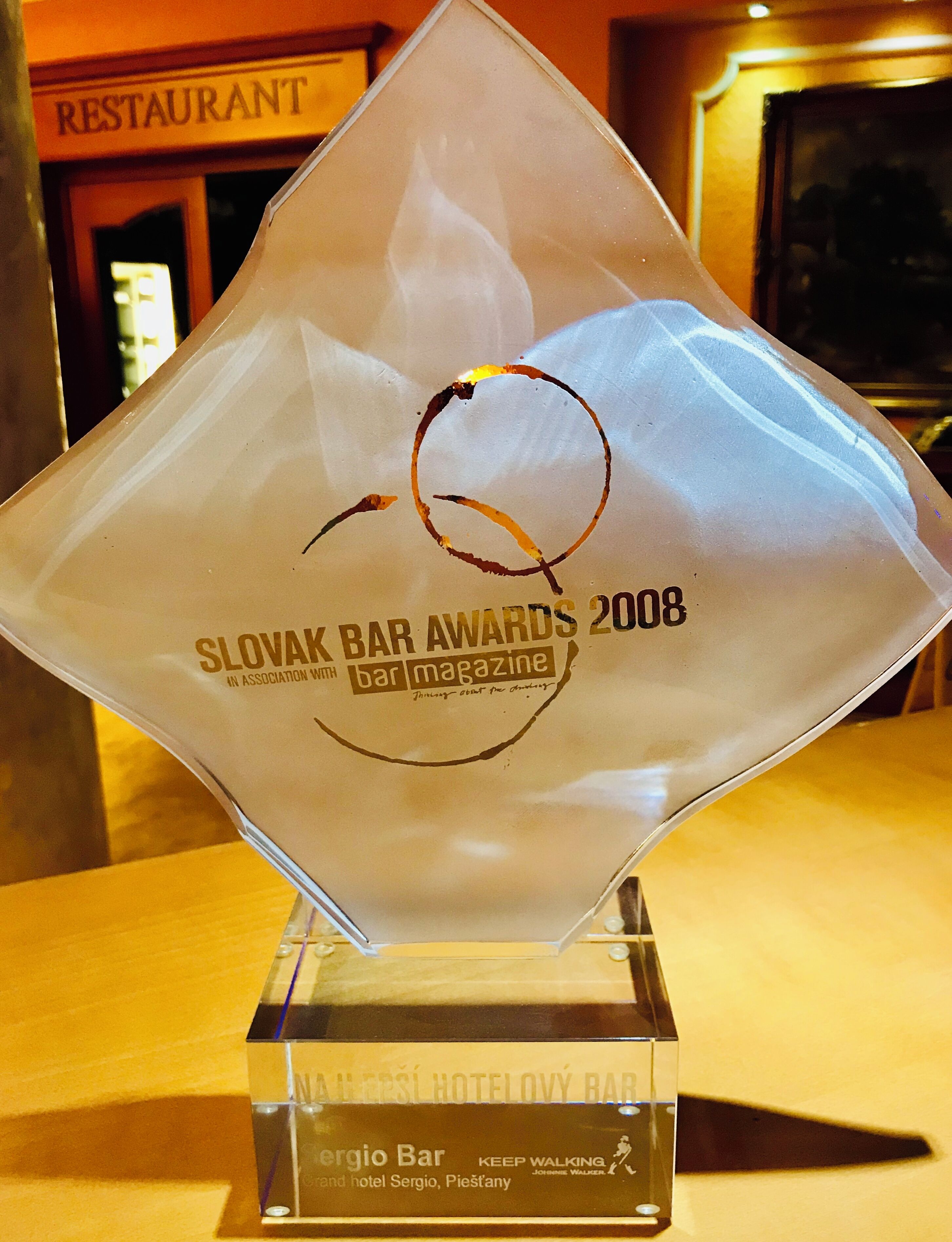 A Slovak Bar Awards 2008 trophy with a circular logo, placed on a clear base.