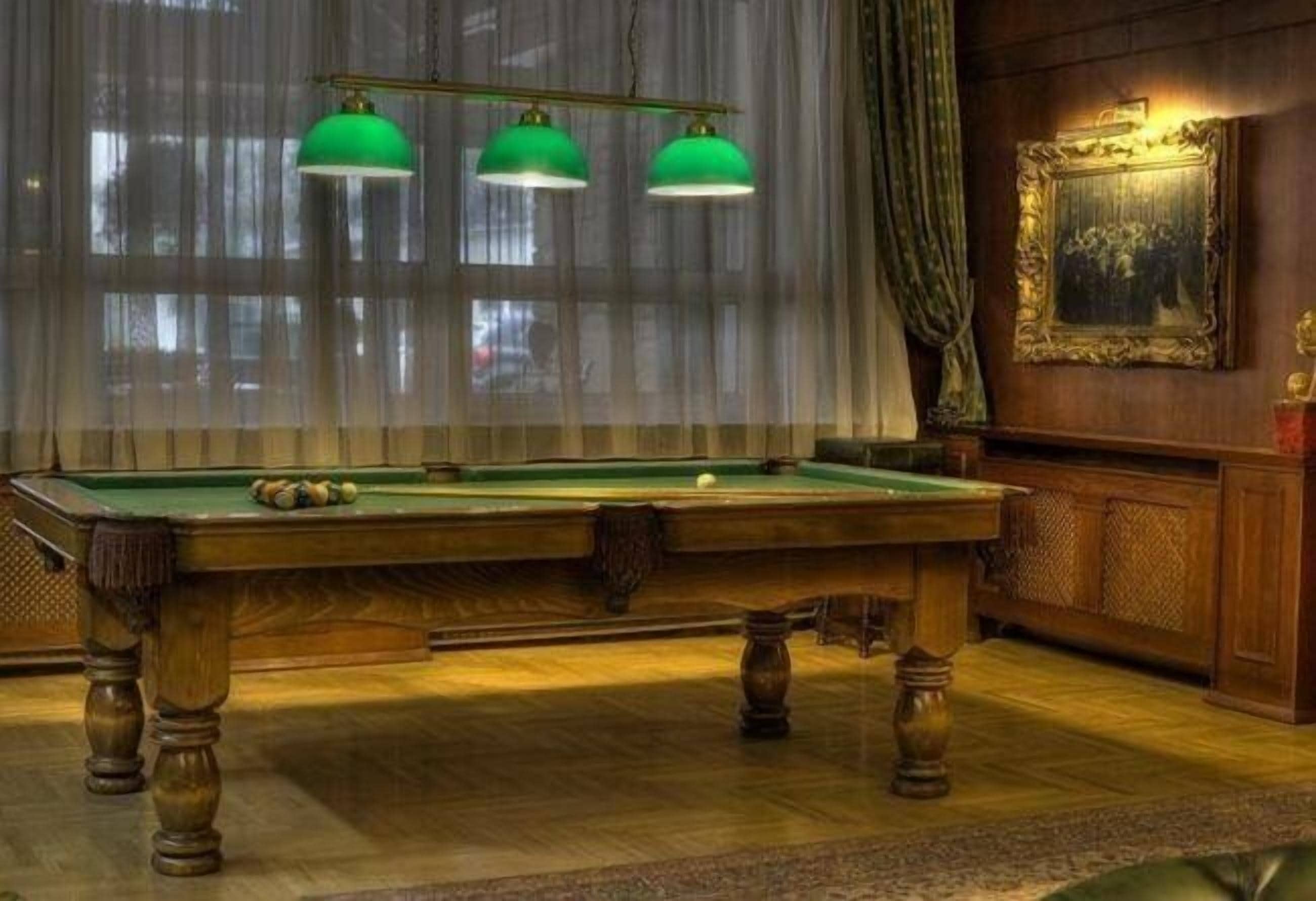 Una mesa de billar con tres lámparas verdes, un cuadro en la pared y un mueble de madera.