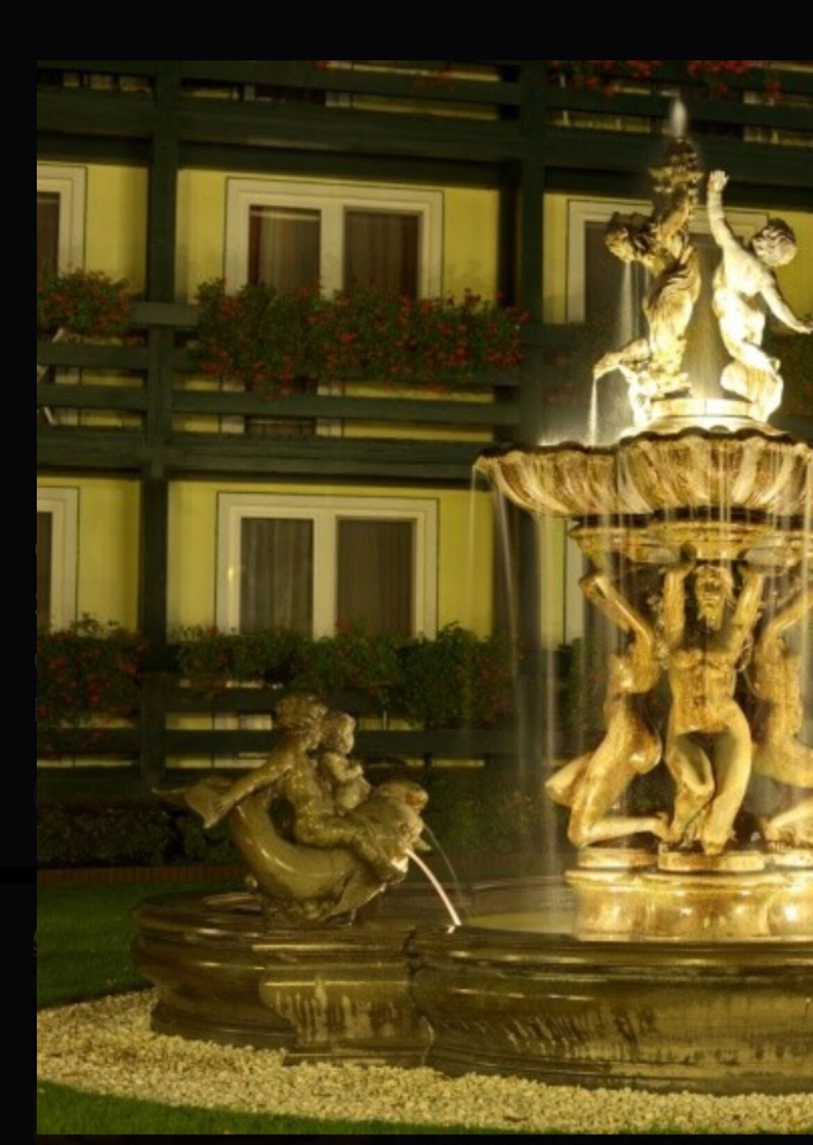 A fountain with classical sculptures in a courtyard with a building in the background.