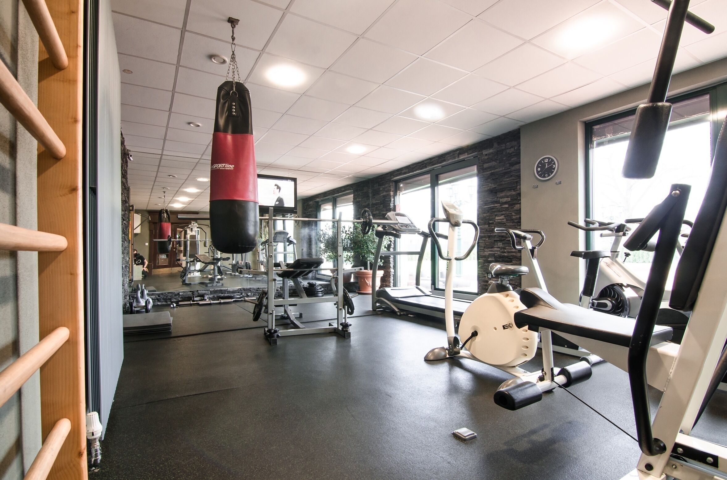 Une salle de sport équipée de divers appareils d’exercice, notamment un sac de frappe, des tapis de course et des appareils de musculation.