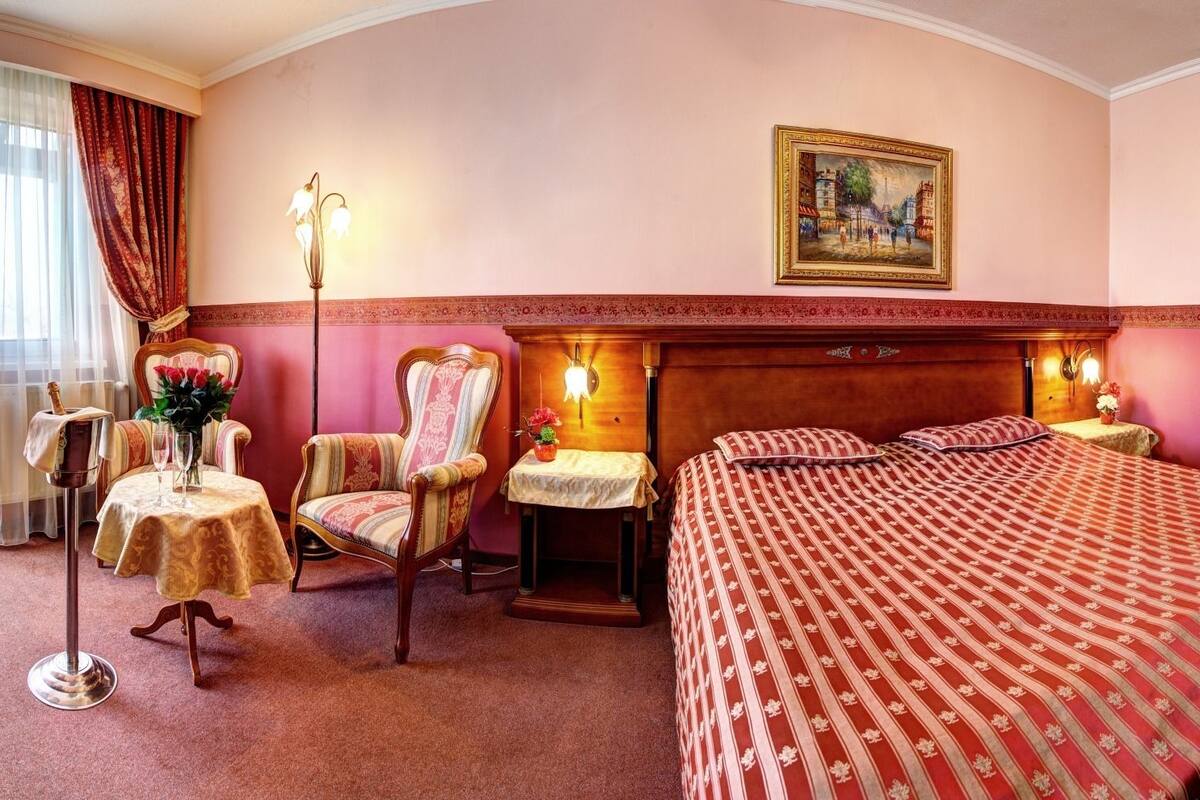 Une chambre d’hôtel avec un grand lit, une chaise, une table ornée d’un vase de fleurs et un tableau accroché au mur.