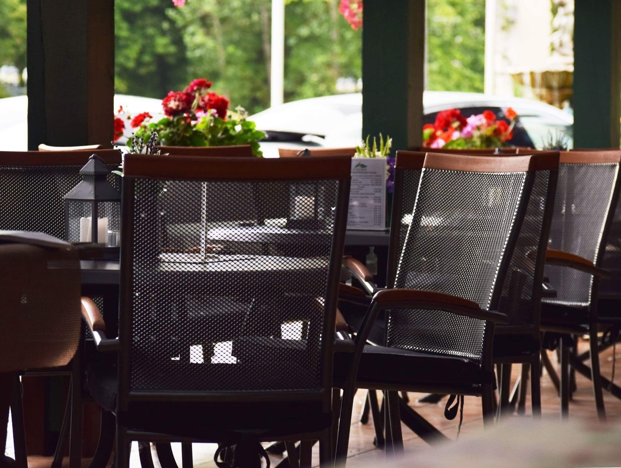 Outdoor dining chairs with mesh backs and wooden armrests, arranged around tables.