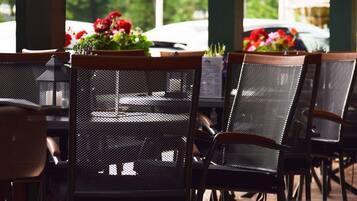 Outdoor dining chairs with mesh backs and wooden armrests, arranged around tables.