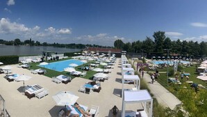 Een zwembadterras met ligbedden en parasols, een groot zwembad en uitzicht op een meer.