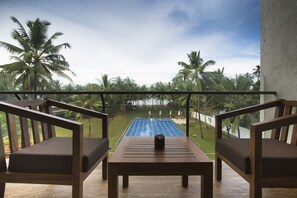 A balcony with wooden furniture and a view of a pool and palm trees. - Taprobana Wadduwa by Asia Leisure (Wadduwa)