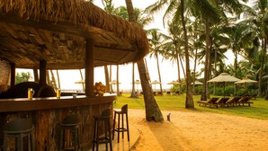 Eine Strandbar mit Reetdach, Holzbarhocker und Meerblick.
