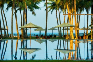 A poolside area with palm trees, umbrellas, and lounge chairs. - Taprobana Wadduwa by Asia Leisure (Wadduwa)