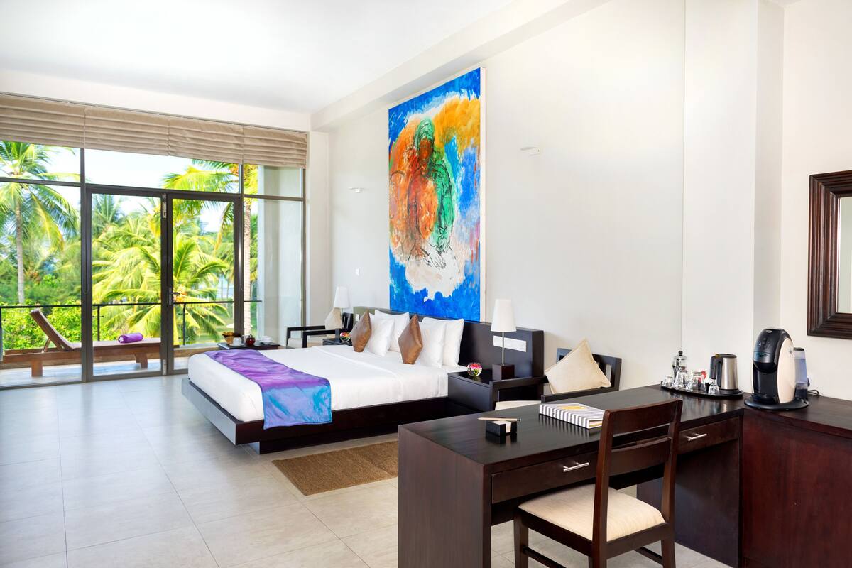 A hotel room with a large bed, a desk, and a view of palm trees.