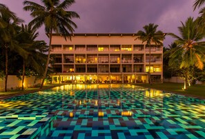 A hotel with a pool featuring a checkered pattern, surrounded by palm trees and a multi-story building with balconies. - Taprobana Wadduwa by Asia Leisure (Wadduwa)