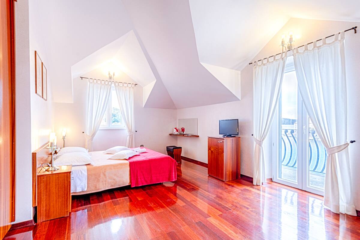A modern bedroom with a bed, bedside tables, a TV, and a balcony with curtains.