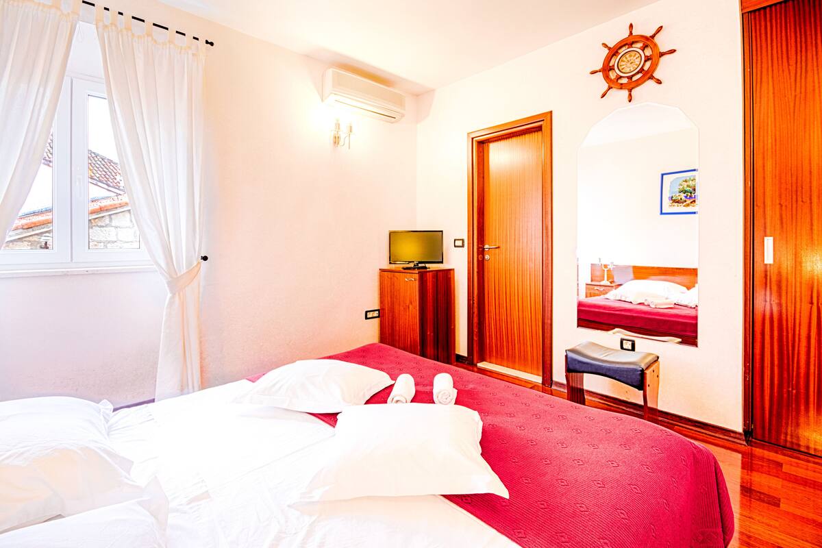 A hotel room with a bed, a television, a wooden wardrobe, a small table, and a window with curtains.