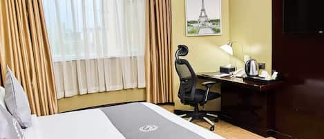 Ein Hotelzimmer mit einem Bett, einem Schreibtisch mit Stuhl, einer Lampe, einem Telefon und einem Bild des Eiffelturms an der Wand.