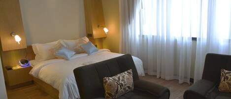 A hotel room with a bed, two bedside lamps, a sofa, and a window with curtains.