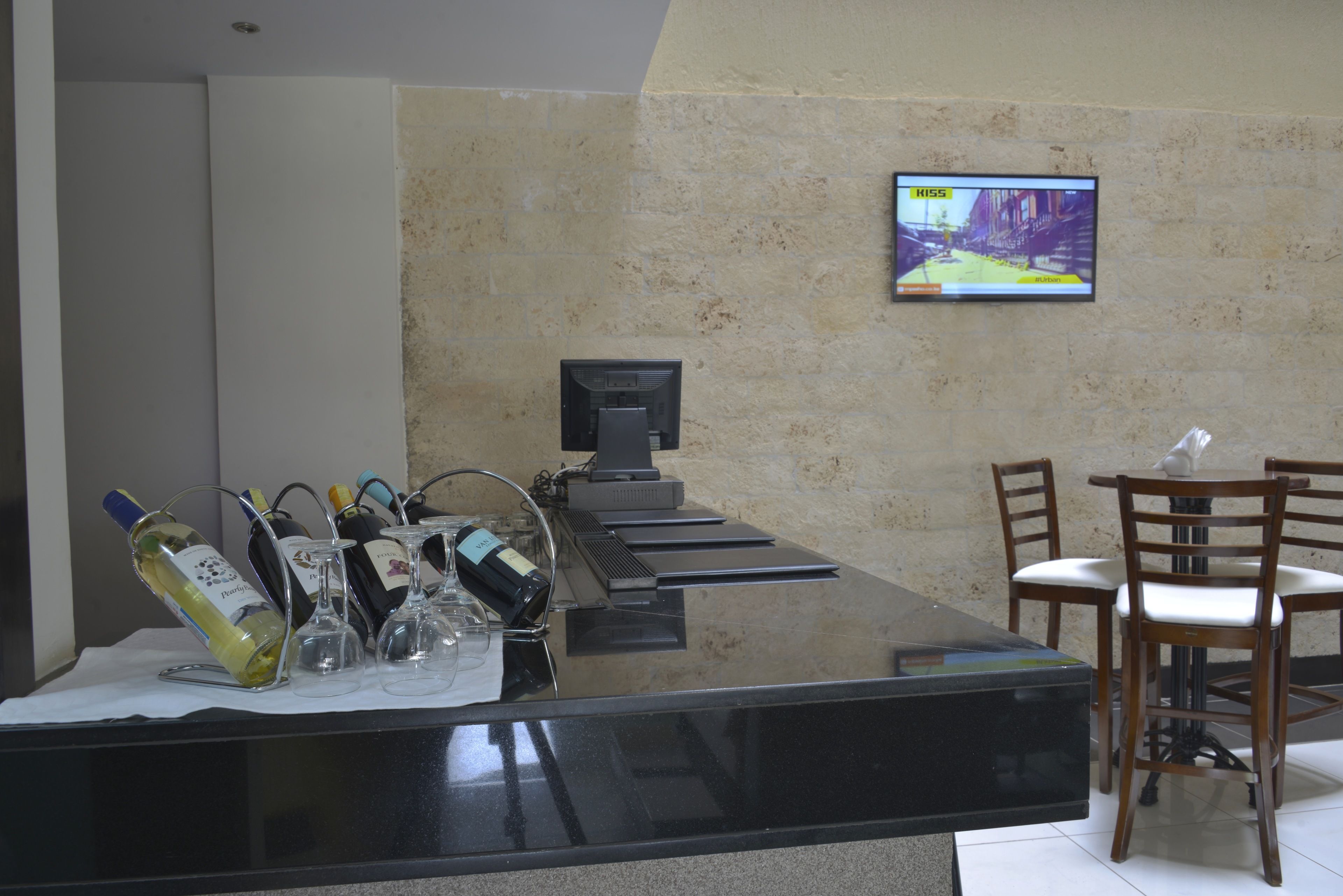 Un espace bar avec un comptoir, des bouteilles de vin, des verres et un écran de télévision diffusant un match.