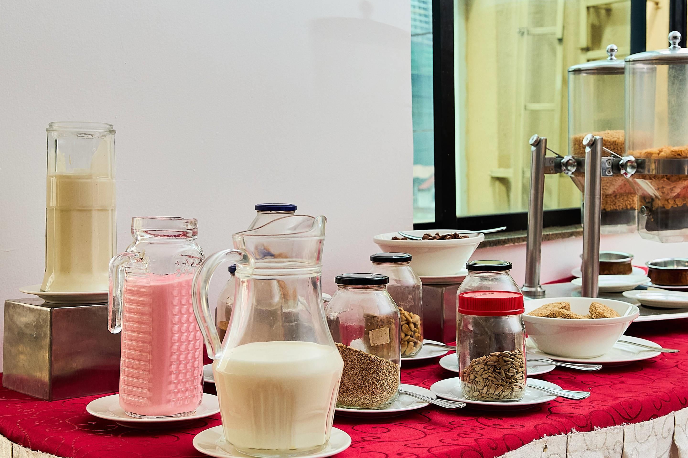 Une table sur laquelle se trouvent divers aliments et récipients, notamment une carafe, une bouteille et des bocaux, probablement pour un service de petit-déjeuner ou de collation.