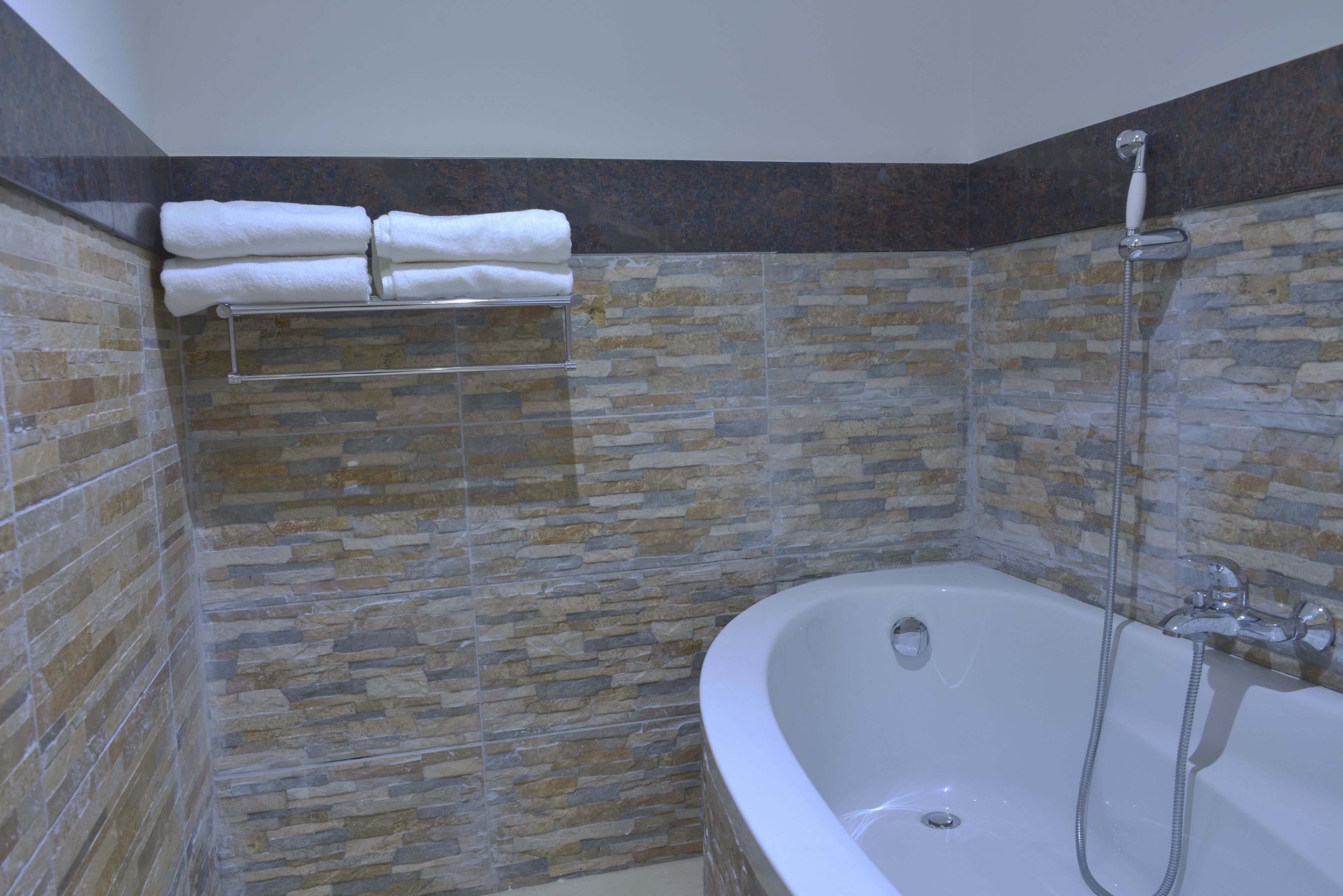 A bathroom with a stone wall, a bathtub, and a towel rack with folded towels.