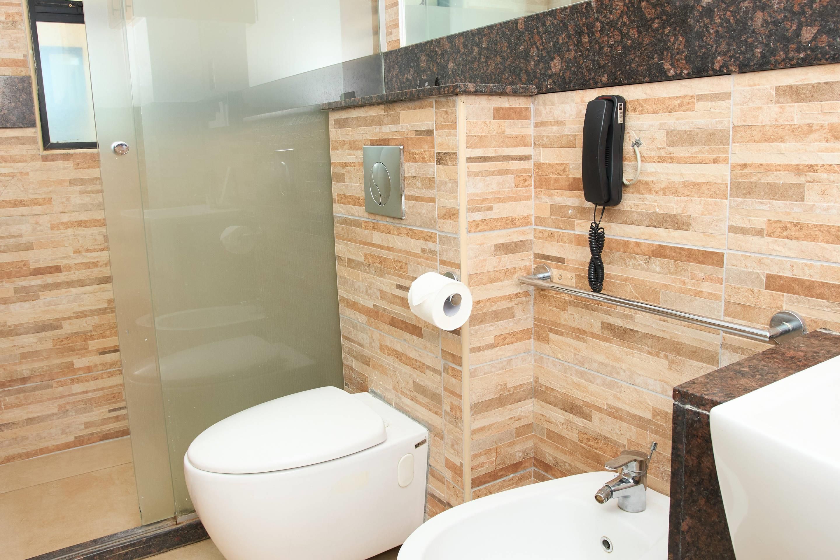 Un baño con inodoro, lavamanos, cabina de ducha de vidrio, toallero y teléfono.