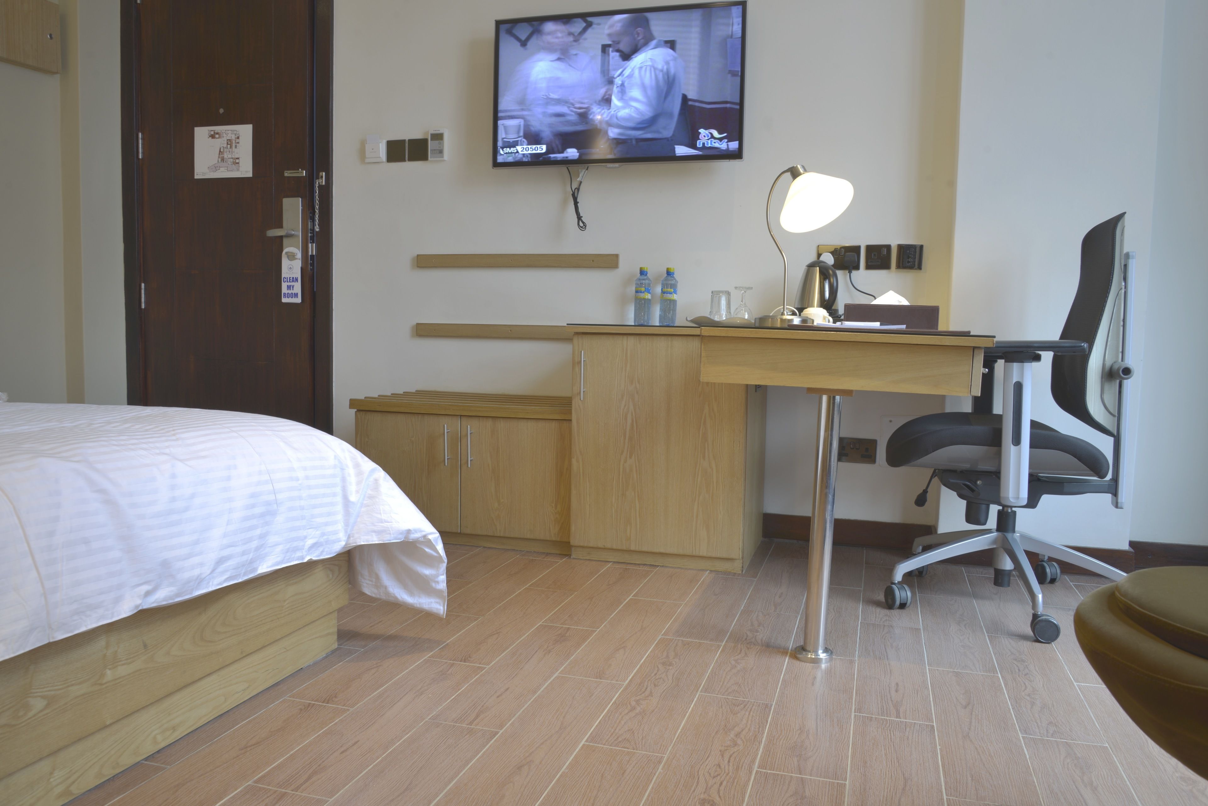 Et hotelværelse med en seng, et skrivebord med stol, et fjernsyn og en skrivebordslampe.