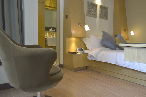 A modern hotel room with a bed, bedside lamps, a nightstand, and a chair. - La Maison Royale - Westlands (Nairobi)