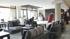 A modern hotel lobby with seating areas, a reception desk, and large windows. - La Maison Royale (Nairobi)