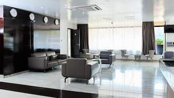Un moderno vestíbulo de hotel con una zona de estar, una recepción y un amplio ventanal con cortinas.