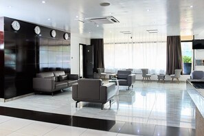 A modern hotel lobby with a seating area, a reception desk, and a large window with curtains. - La Maison Royale - Westlands (Nairobi)