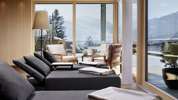 A modern room with a large window, a sofa, a lamp, and a view of mountains. - Natur Resort RISSBACHER (Stumm)