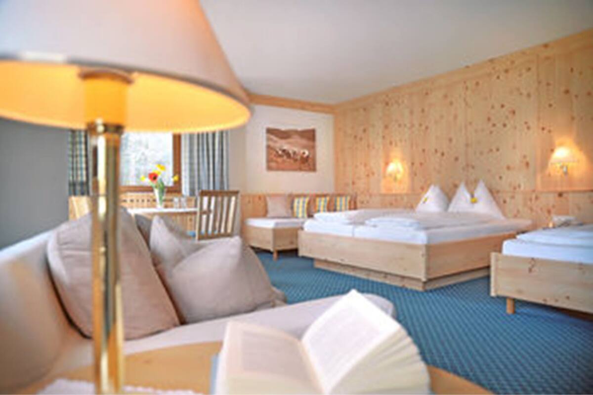 A hotel room with a large bed, a sofa, a reading area, and a view of the outdoors.