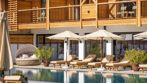 A pool area with lounge chairs, umbrellas, and a wooden deck. - Natur Resort RISSBACHER (Stumm)
