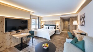 A modern hotel room with a large bed, a desk, a TV, and a bowl of fruit on the coffee table. - Natur Resort RISSBACHER (Stumm)
